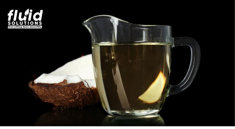 Transparent pitcher with coconut oil beside a halved coconut.