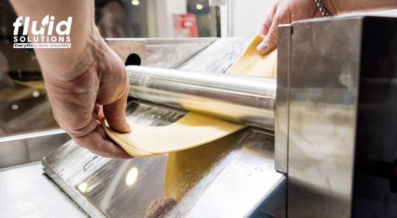 Hands guiding dough through a pasta machine.