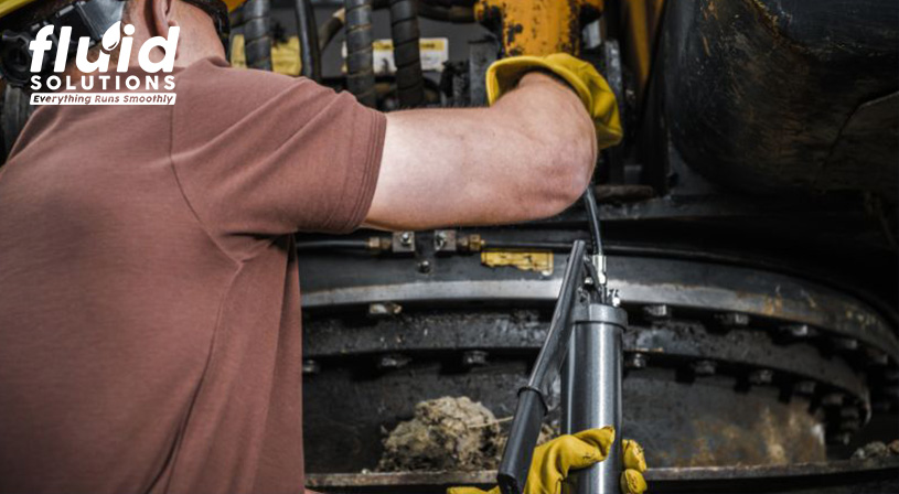 Worker using a grease gun on industrial machinery.