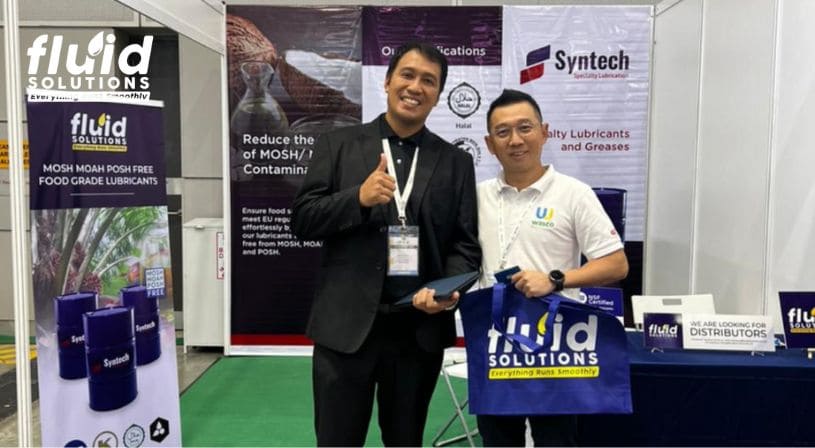 Two men posing at the Fluid Solutions trade show booth, one holding a branded bag."