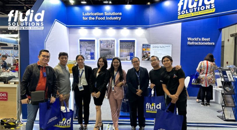 Fluid Solutions team posing with trade show attendees carrying branded bags.