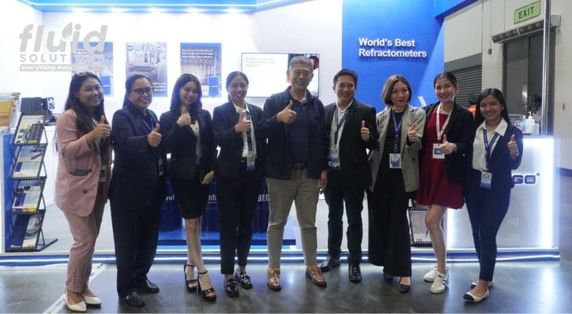 Group of Fluid Solutions team members and attendees posing with thumbs up at a trade show booth.