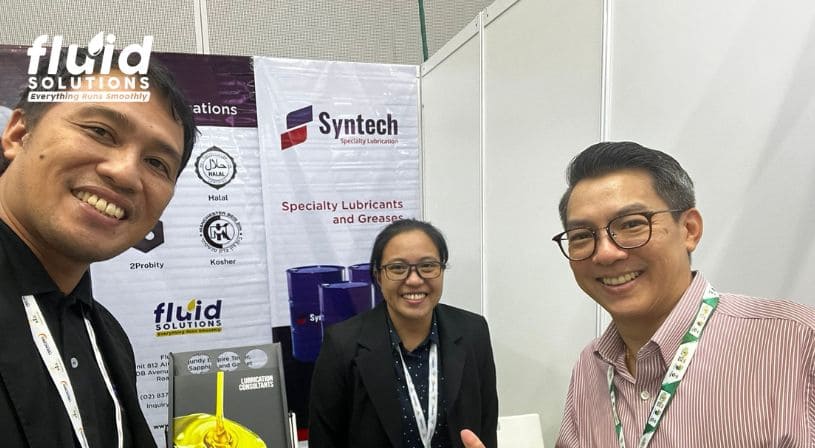 Group selfie of Fluid Solutions representatives at a trade show booth featuring Syntech specialty lubricants.