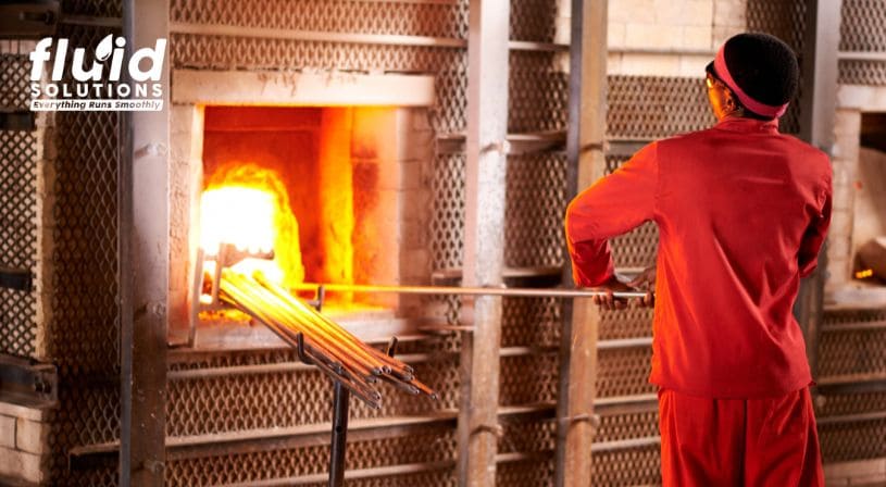 Worker in protective gear operating a furnace in a foundry.