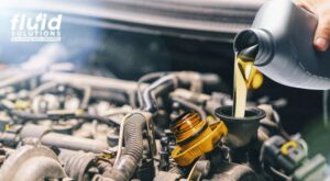 Mechanic pouring engine oil into a car engine with the Fluid Solutions logo in the background.