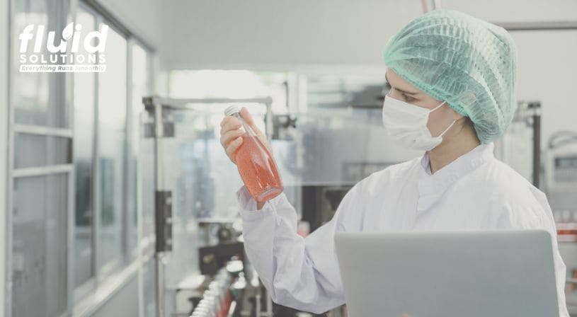 Quality control worker inspecting a beverage bottle in a food processing plant, wearing protective gear