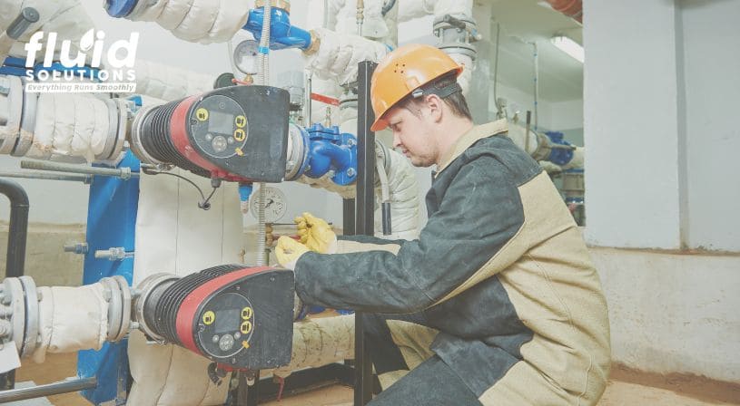 Worker performing maintenance on industrial pipes and valves while wearing safety gear