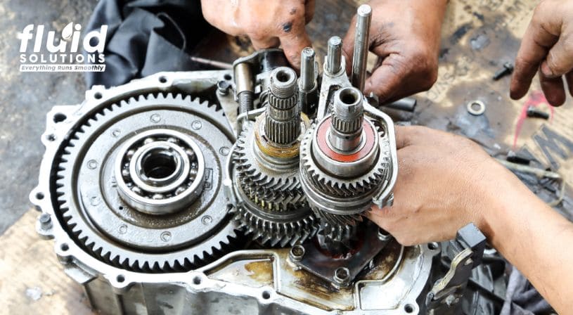 Close-up of a mechanic working on a transmission assembly with visible gears