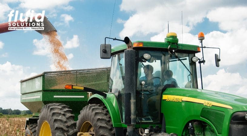 Green tractor unloading harvested grain in a field.