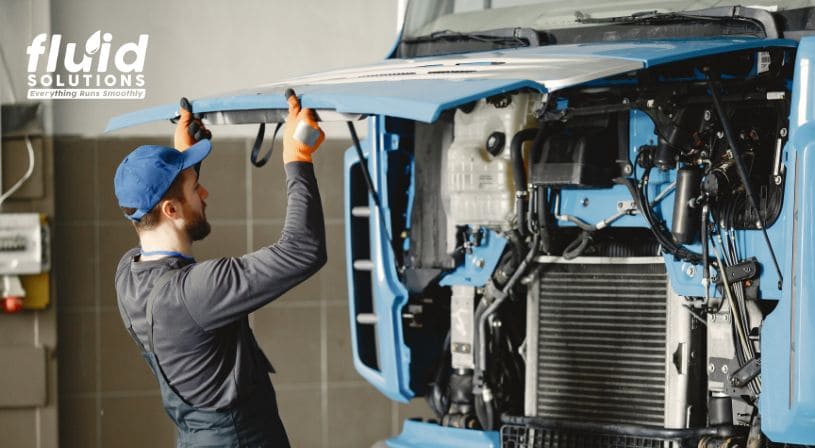 Mechanic inspecting the engine of a blue truck.