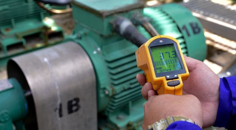 Technician using an infrared thermometer to measure the temperature of a green industrial motor.