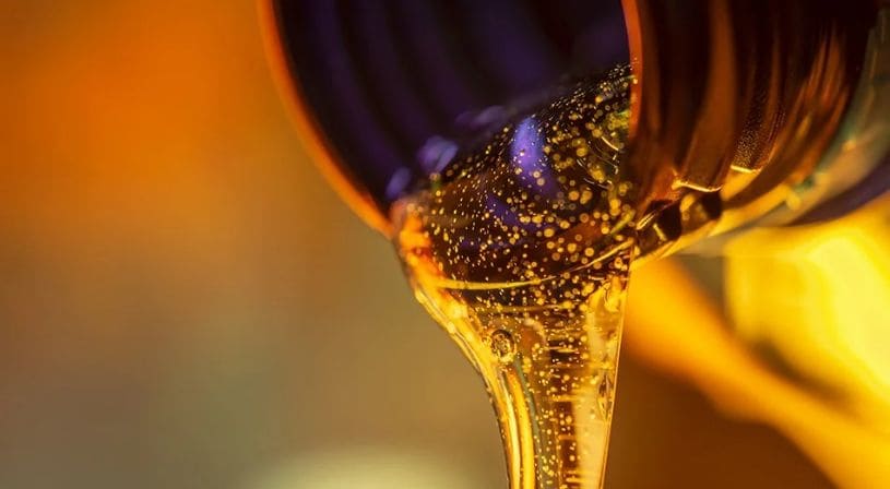 Close-up of golden, viscous lubricant being poured from a container.