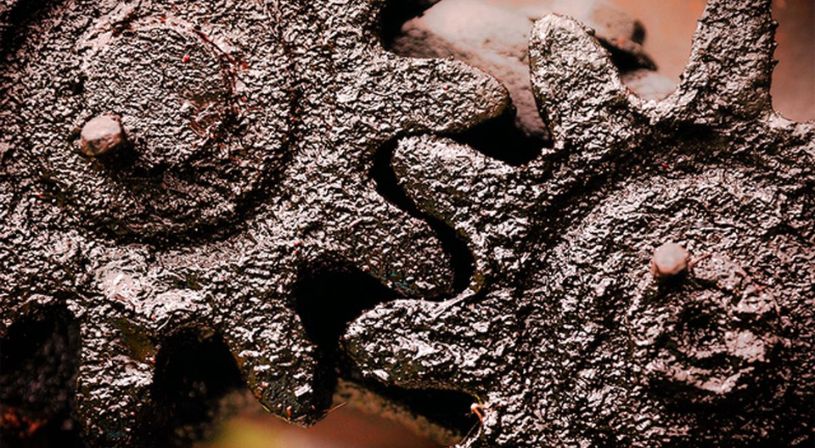 Two metal gears covered in thick, black, degraded grease, indicating wear and contamination.